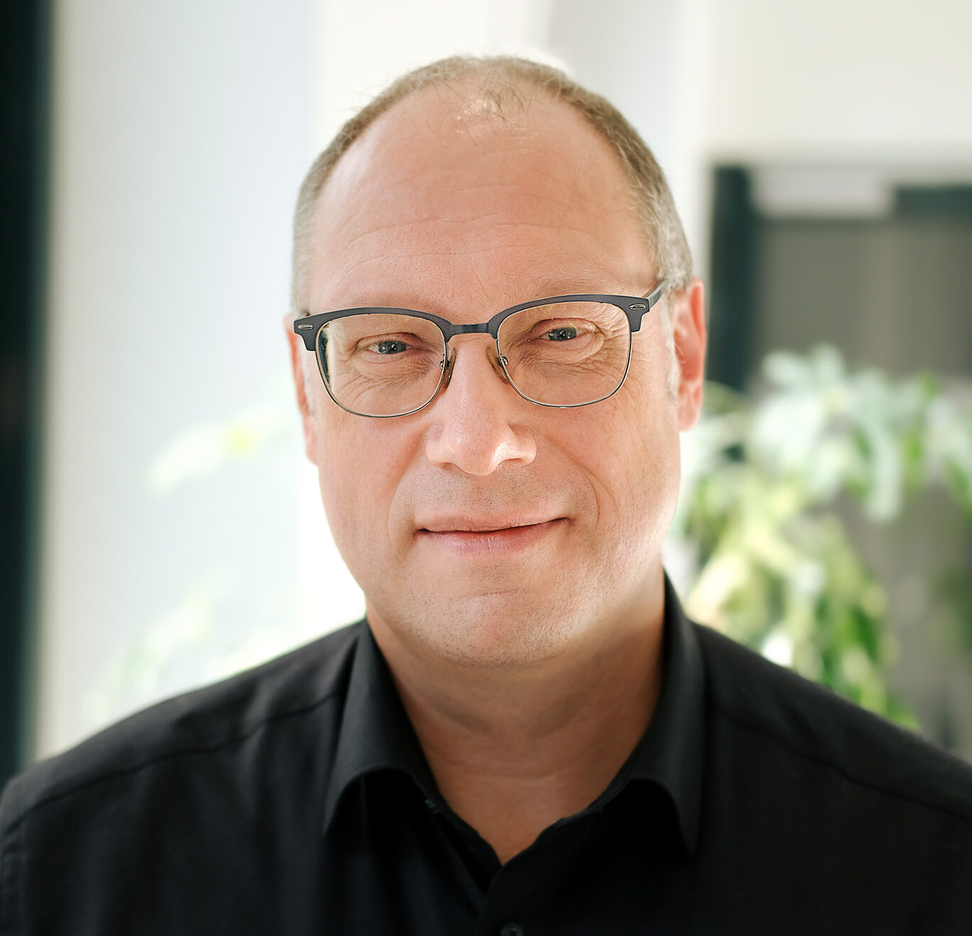 Ein Portrait von Markus Sextro, Geschäftsführer der SNS Connect GmbH, im schwarzen Hemd mit Brille